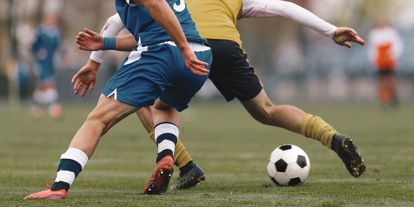 Foto: Zwei Fußballspieler auf dem Fußballfeld kämpfen um den Ball.