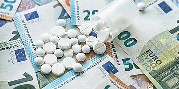 Tabletten liegen auf Geldscheinen.
