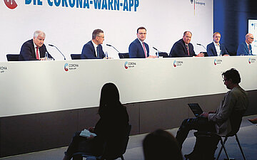 Foto: Konferenz zur Vorstellung der Corona-Warn-App mit Menschen auf Podium