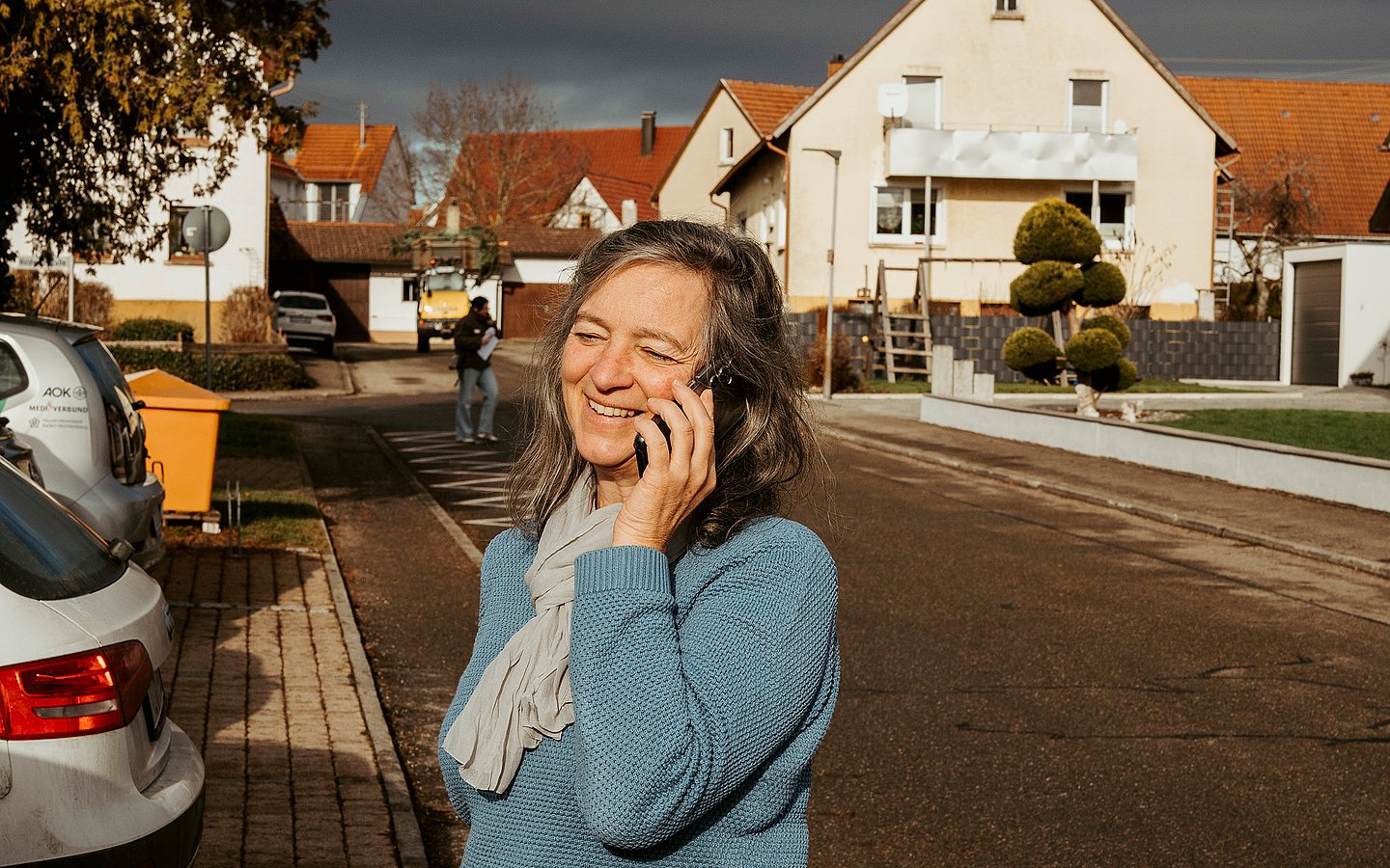 Foto von Patientenlotsin Veronika Hermle-Wehl mit Handy neben ihrem Auto