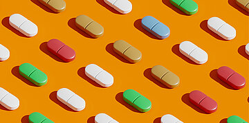 Mehrere verschiedenfarbige Tabletten sind regelm&auml;&szlig;ig auf einem orangefarbenen Hintergrund angeordnet.