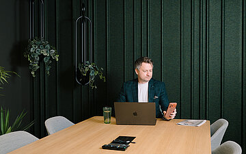 Foto: Prof. Dr. David Matusiewicz mit Laptop und Smartphone an einem gro&szlig;en Konferenztisch.