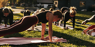 Foto: Eine Gruppe trainiert gemeinsam im Freien und st&uuml;tzt sich auf Yogamatten ab.