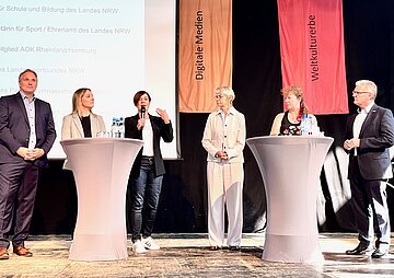 Gemeinsamer Auftritt f&uuml;r das Sporthelfer-Programm: Vertreterinnen und Vertreter aus Politik, Sport, Schule und Krankenversicherung, darunter Sabine Deutscher (am Mikrofon), Vorst&auml;ndin der AOK Rheinland/Hamburg