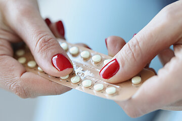 Zwei rot lackierte Frauenh&auml;nde halten einen Blister mit einer Antibabypille.