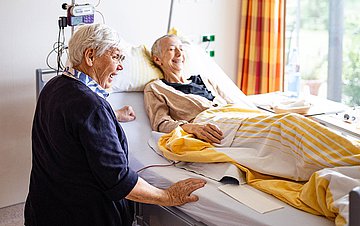 Foto: Stimmtherapeutin, Renate Aug (links), sitzt am Bett von Frau S.