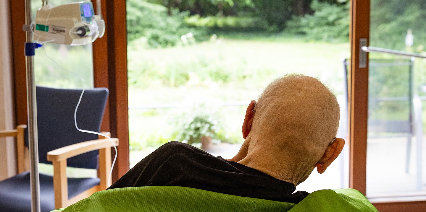 Foto: Ein Mann sitzt in einem Zimmer auf der Palliativstation im Rollstuhl und schaut Richtung Fenster.