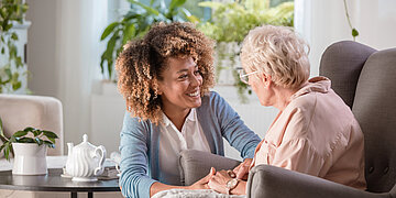 Eine junge Frau spricht mit einer &auml;lteren Frau, die im Sessel sitzt.