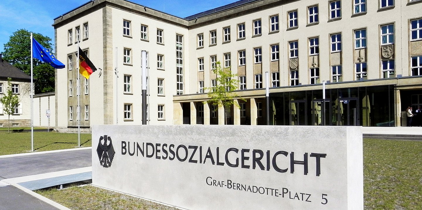 Das Foto zeigt den Eingangsbereich zum Gebäude des Bundessozialgericht. Eine große Steintafel steht auf dem Boden mit dem Schriftzug des Bundessozialgerichts mit dem Bundesadler.