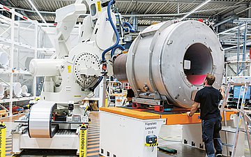 Foto: In einer großen Maschinenhalle: ein MRT Gerät wird von einem Maschinenbauer inspiziert