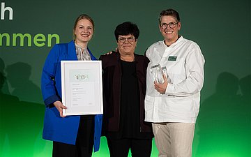 Drei Personen stehen nebeneinander mit Urkunde und Preis.