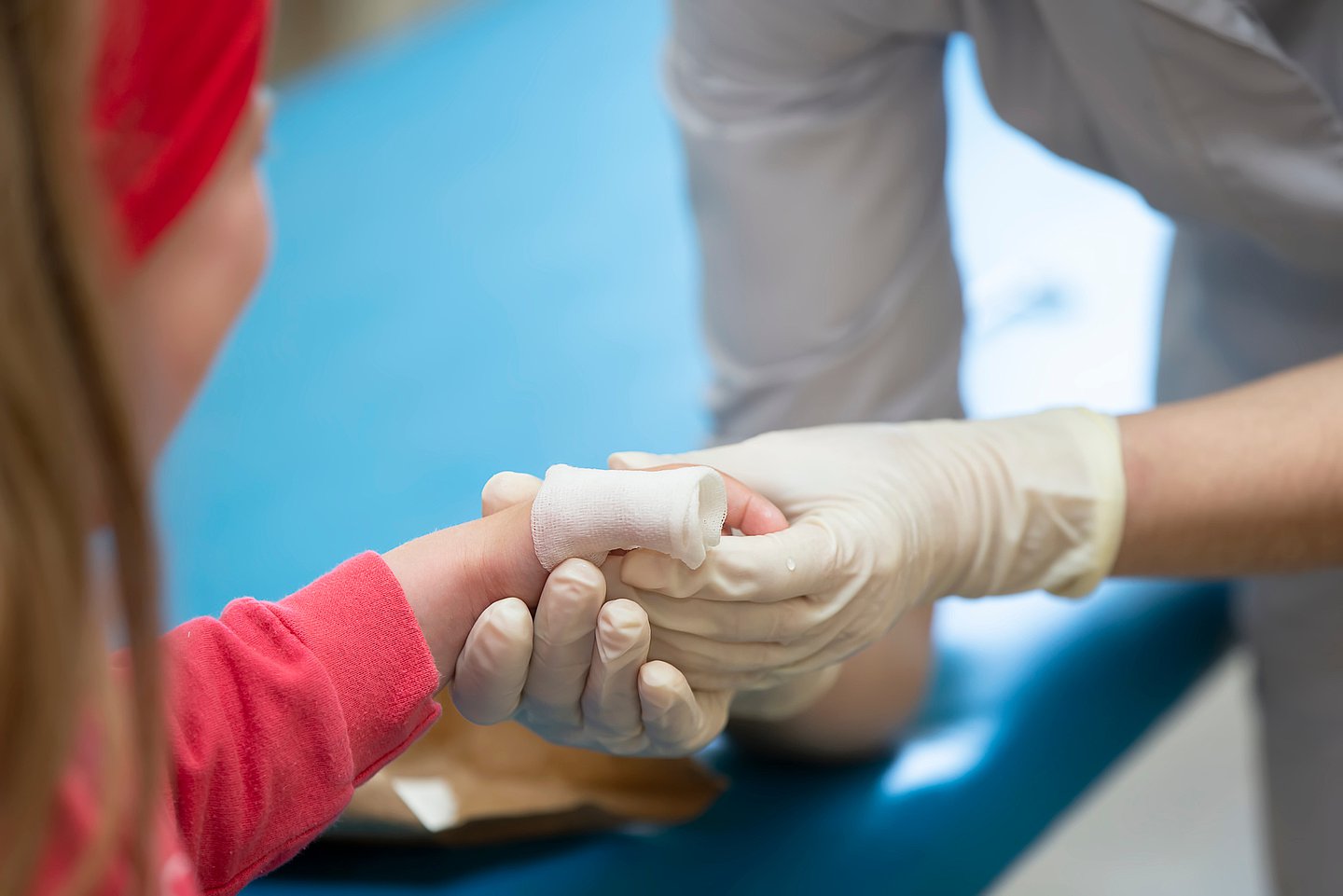 Das Foto zeigt ein Kind mit Verbrennungen an der linken Hand, das von medizinischem Personal behandelt wird.