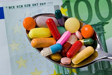 Mehr Geld für Arzneimittel Ein Löffel mit verschiedenen Medikamenten liegt über einem Hundert-Euro-Geldschein.