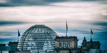 Die Kuppel und die Türme des Bundestagsgebäudes heben sich vor einem abendlichen blauen Himmel ab.