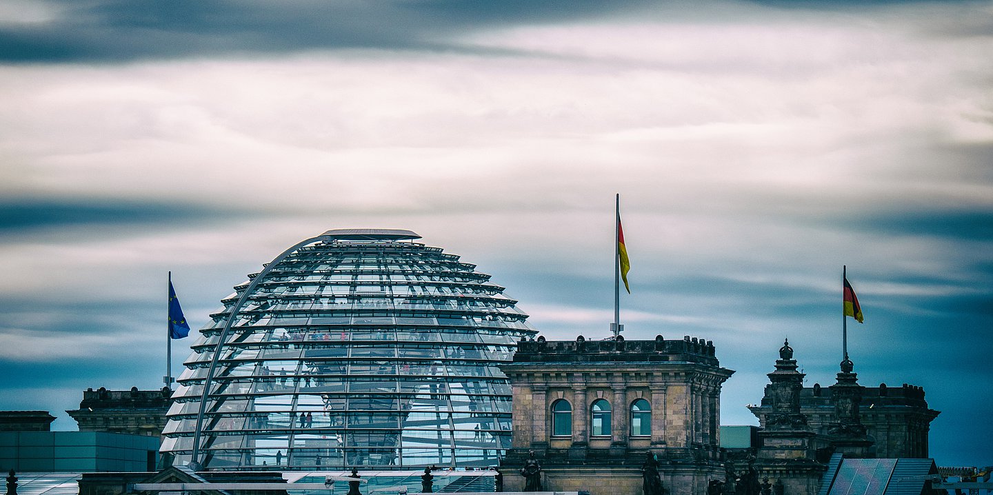 Die Kuppel und die Türme des Bundestagsgebäudes heben sich vor einem abendlichen blauen Himmel ab.