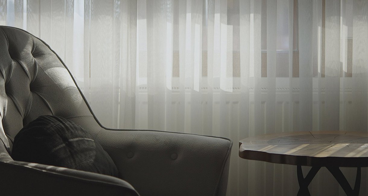 Foto: Ein grauer Sessel steht in einem dunklen Zimmer vor zugezogenen Gardinen.