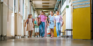 Foto: Sch&uuml;lerinnen und Sch&uuml;ler laufen gemeinsam lachend durch einen Schulflur.