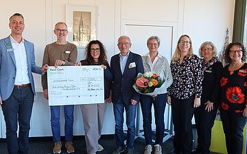 Gruppenfoto mit acht Personen und einem großen Scheck zur Spendenübergabe an das Aufschnaufhaus in Ulm.