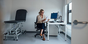 Eine Frau sitzt an ihrem Arbeitsplatz und schaut sich Unterlagen an.