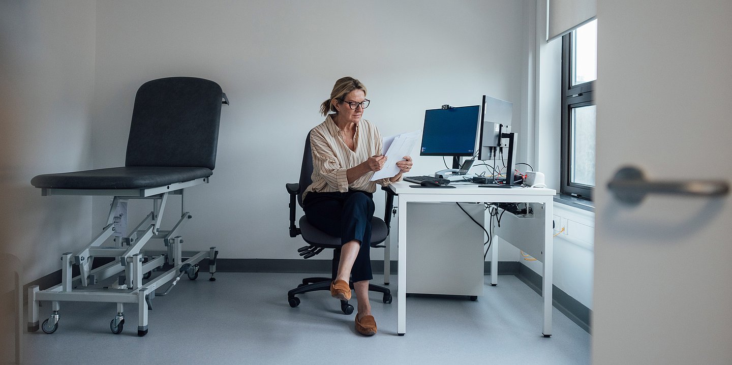 Eine Frau sitzt an ihrem Arbeitsplatz und schaut sich Unterlagen an.