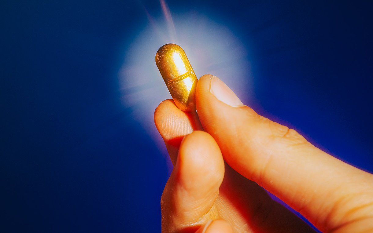 Close Up auf eine Hand, die eine goldene Pille hoch hält, im Hintergrund ein Heiligenschein.