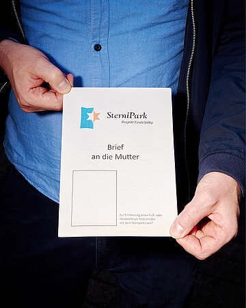 Ein Mann h&auml;lt ein St&uuml;cke Papier in der Hand. Auf ihm steht SterniPark (Project Findelbaby) - Brief an die Mutter.
