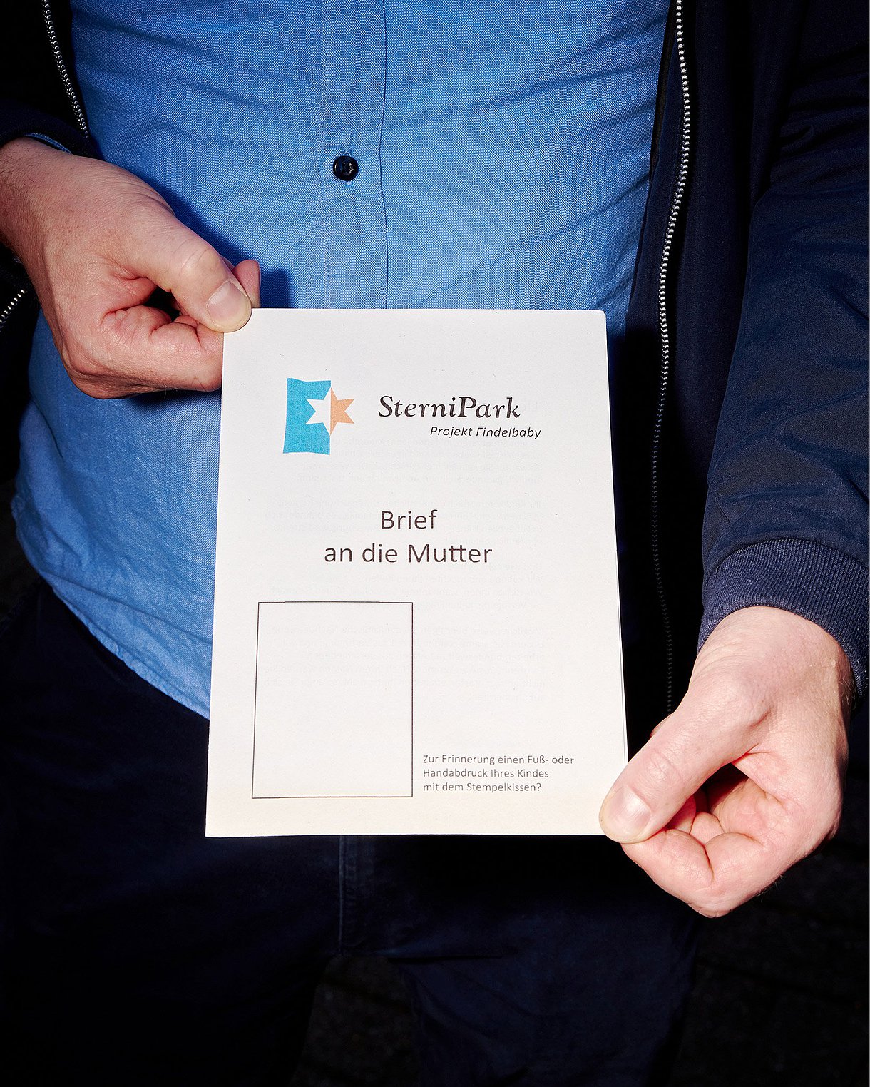 Ein Mann hält ein Stücke Papier in der Hand. Auf ihm steht SterniPark (Project Findelbaby) - Brief an die Mutter.