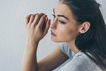 Klinikeinweisungen wegen Depressionen in Schleswig-Holstein Eine junge Frau sitzt irgendwo; sie schaut traurig betrübt ins Leere, die Hände hält sie zusammengelegt locker vor dem Gesicht.