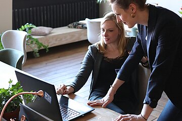 Zwei Frauen schauen auf einen Laptop auf einem Tisch.
