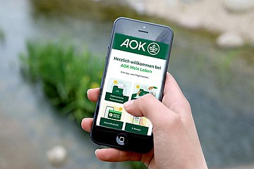 Integration E-Rezept Eine Hand hält ein Smartphone, auf dem eine AOK-App läuft.