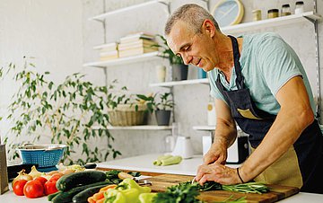 Gesunde Ernährung Ein Mann steht in der Küche und schneidet Gemüse.