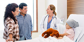 Eltern stehen mit einer &Auml;rztin am Krankenbett ihres Kindes. 