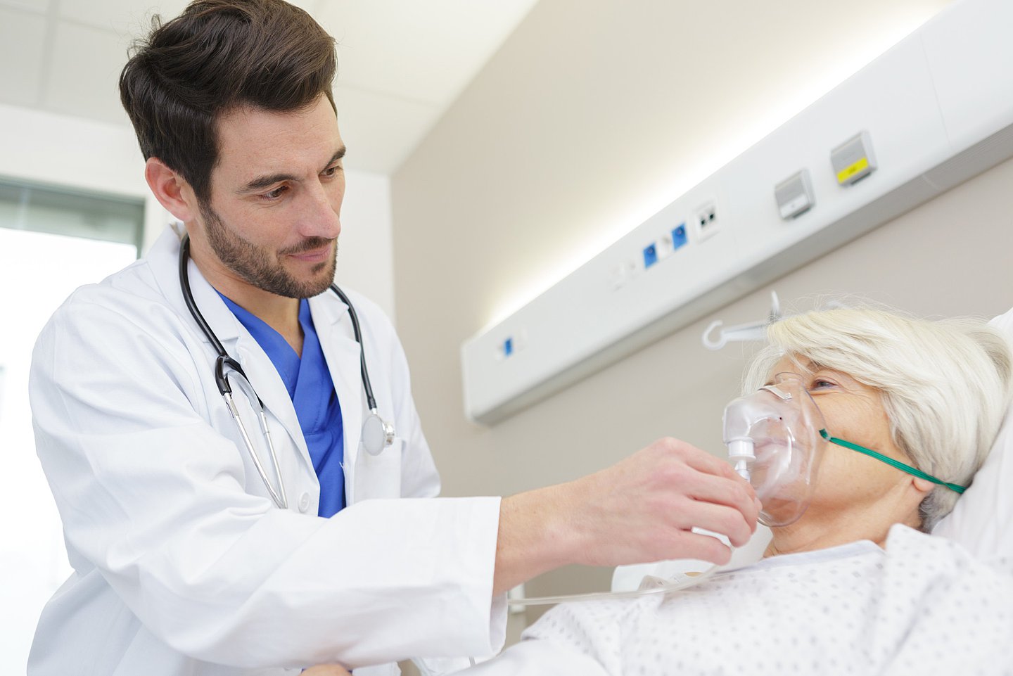 Das Foto zeigt einen Arzt im Krankenhaus, der bei einer Patientin eine Sauerstoffmaske anlegt.