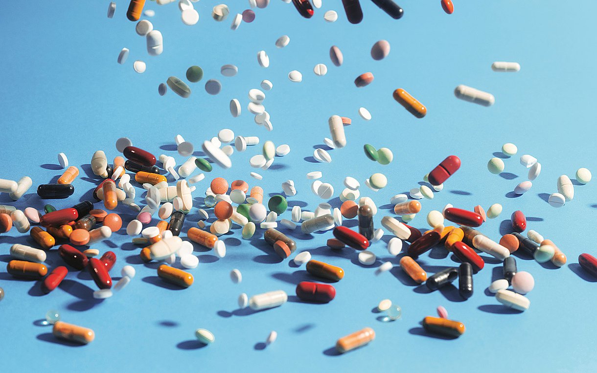 Foto von rieselnden bunten Tabletten. Viele liegen schon auf einem hellblauen Untergrund