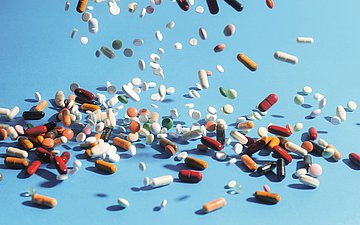 Arzneimittel Foto von rieselnden bunten Tabletten. Viele liegen schon auf einem hellblauen Untergrund