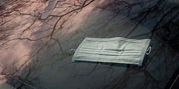 Foto: Eine medizinische Maske, daneben spiegeln sich Äste eines Baumes.