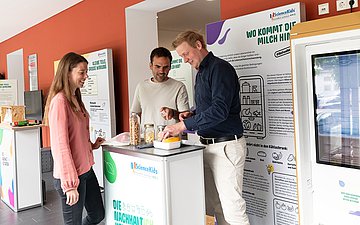 Eine Frau und zwei Männer betrachten lächelnd einen Gegenstand