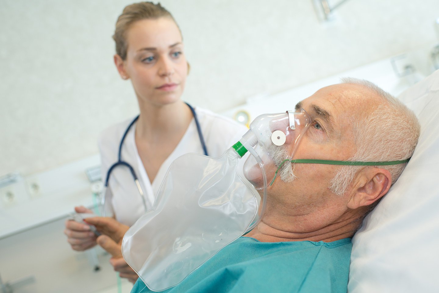 Das Foto zeigt eine Ärztin im Krankenhaus, die bei einem älteren Patienten eine Sauerstoffmaske anlegt.