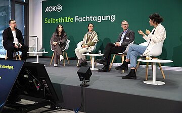F&uuml;nf Personen sitzen bei dieser Podiumsdiskussion nebeneinander auf St&uuml;hlen, die im Halbkreis arrangiert sind. 