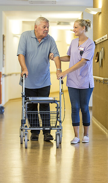 Eine Pflegerin begleitet einen Patienten mit einem Rollator