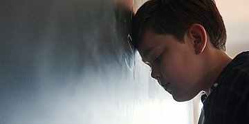 Leistungsangst bei Kindern Foto: Ein Junge lehnt mit dem Kopf und geschlossenen Augen an einer Tafel.