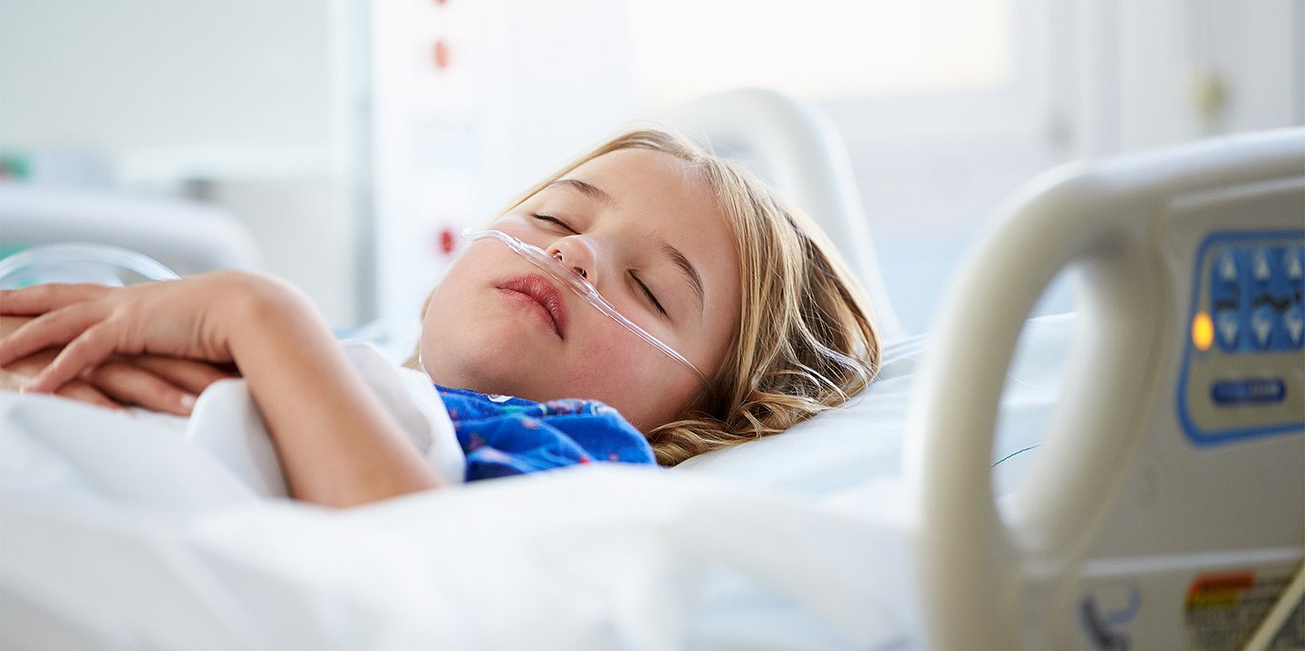 Das Foto zeigt ein Kind, das in einem Krankenhausbett liegt.