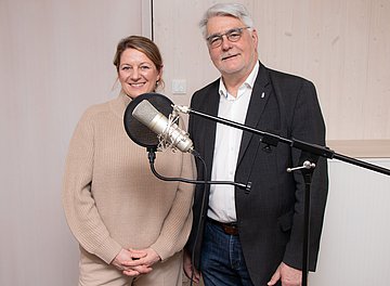 Podcast zum GKV-Rekorddefizit AOK-Landesdirektorin Iris Kröner und der Präsident der Ärztekammer Schleswig-Holstein Prof. Henrik Herrmann stehen vor einem Aufnahmemikrofon.
