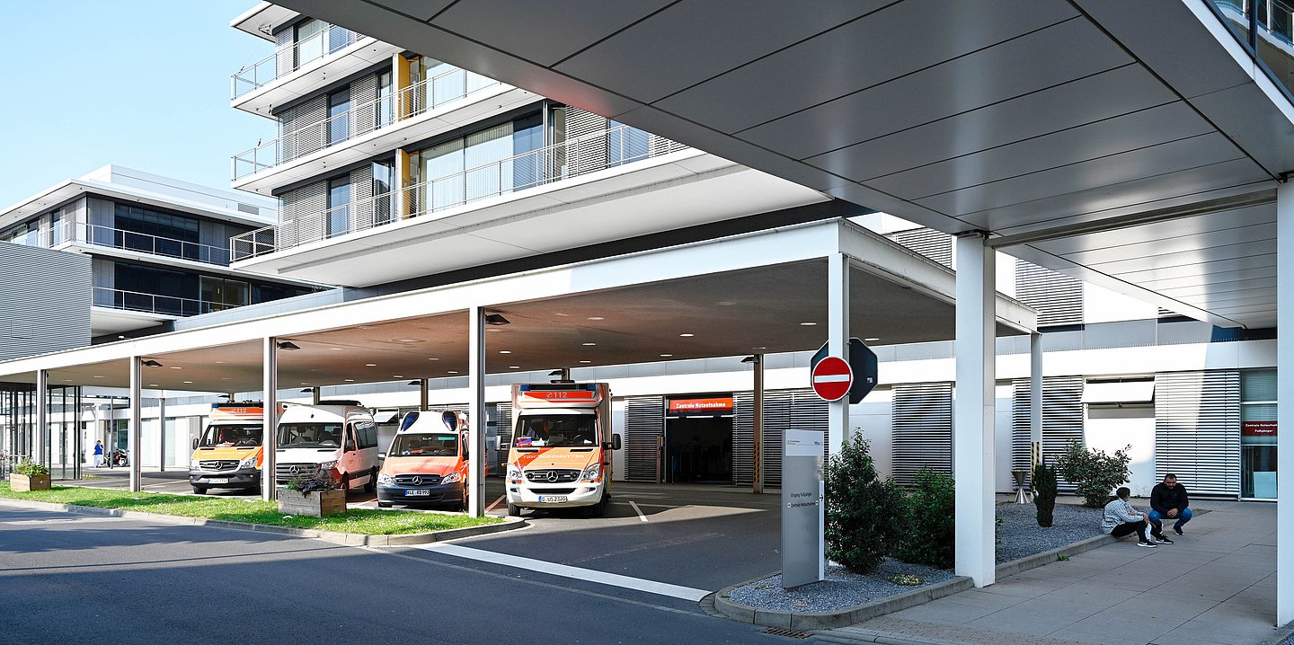 Foto: Blick auf mehrere Rettungswagen in einer Einfahrt eines Krankenhausses nähe der Notaufnahme