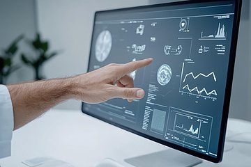 Eine linke Hand zeigt auf einen Computerbildschirm, auf dem verschiedene Grafiken angezeigt werden.