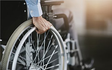 Hilfsmittel Rollstuhl Foto: Hand des Fahrers bewegt Rad eines Rollstuhls.