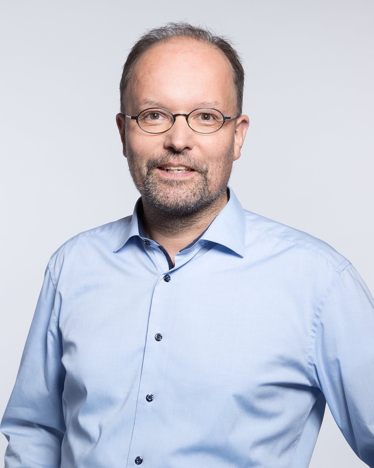 Porträtfoto zeigt Kopf und Rumpf, Ralf Metger trägt eine ovale Brille und ein hellblaues Hemd.