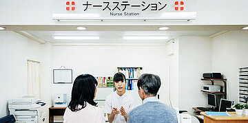 Foto: Ein Mann und eine Frau stehen einer Gesundheitsfachkraft oder &Auml;rztin gegen&uuml;ber.