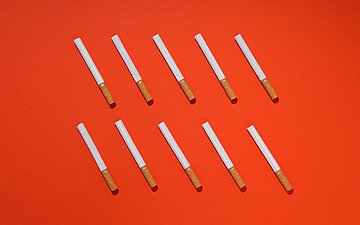 Foto: Mehrere Zigaretten liegen nebeneinander auf einem roten Untergrund.