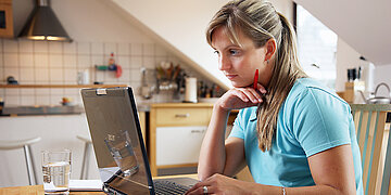 Junge Frau, die sich in der heimischen K&uuml;che an einem Laptop informiert